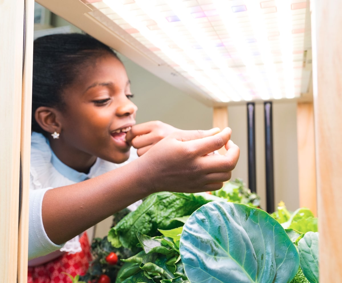 Young girl snacking on fresh produce from her Rise Garden, excited and having fun enjoying the fruits of her family’s indoor gardening efforts.