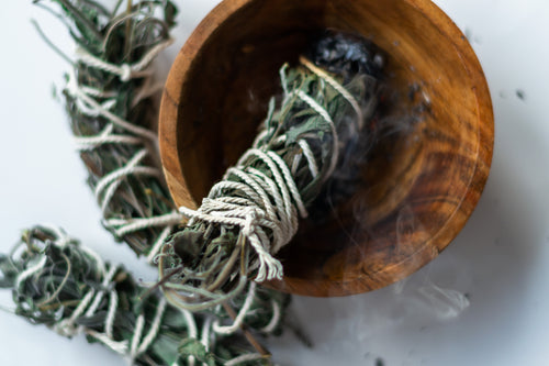 sage smudge stick in a wooden bowl with sage smudge sticks around it