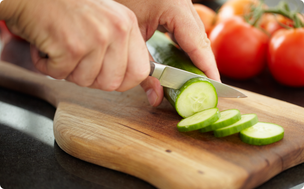 Hands slicing cucumber on board